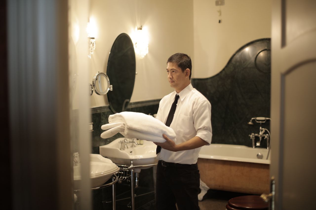 services-04 Side view of young male employee holding stack of white towels while standing in bathroom of luxury hotel